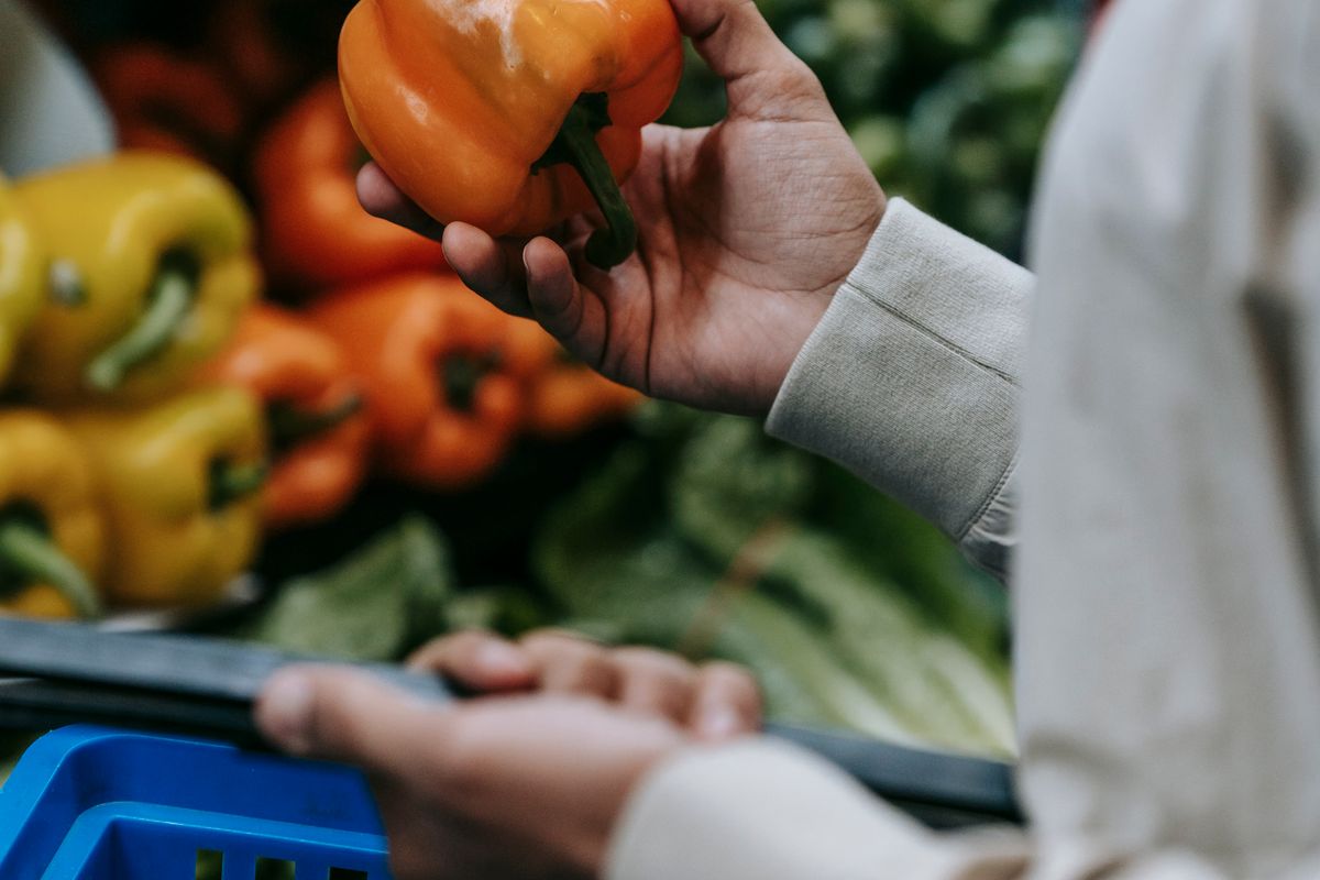 A customer choosing fresh vegetables with a shopping basket in the convenience shop